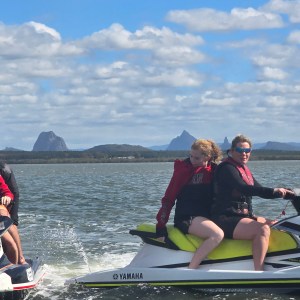 Two people on jet skis riding on a lake under a cloudy sky.