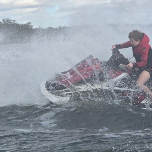 Two people riding a jet ski in choppy water, creating a large splash.