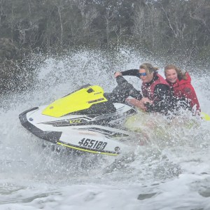 Two people riding a jet ski through splashing water.